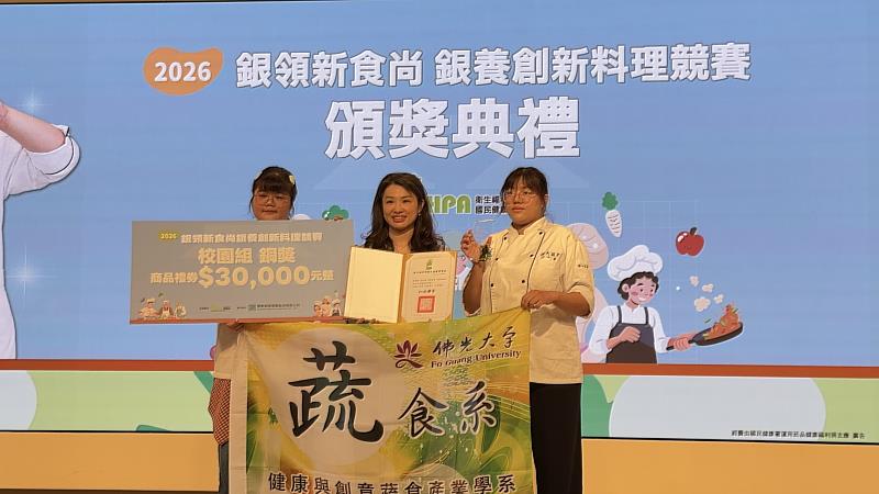 國民健康署沈靜芬署長(中)頒發校園組銅獎的獎項給佛大蔬食系學生李佩穎(右)、盧以倢(左)。
