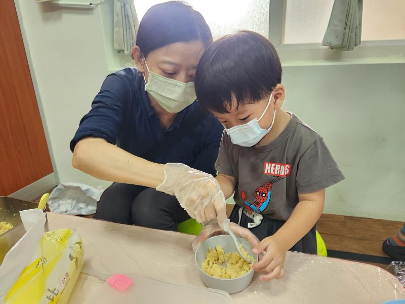 家長帶著孩子一起將綠豆仁攪拌成泥。
