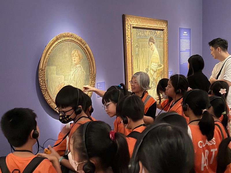 七賢國小美術班學生邊聽導覽，邊觀察慕夏作品的線條與色彩。／時藝多媒體提供