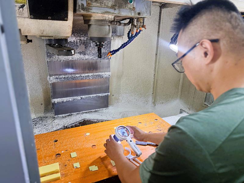 小吳於機台加工區使用手持式燈光照明放大鏡,克服現場環境光線與微小細節限制,確保精密加工品質。