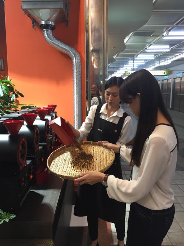  
體驗烘豆教學的民眾在咖啡樹旁開心的持竹篩為剛烘好的咖啡豆去銀皮。