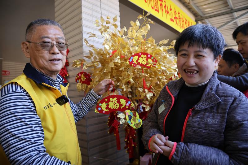 昇恆昌免稅商店董事長江松樺（左）親手寫上新年祝福，和「安康啟智教養院」院生一起掛在發財樹吊飾。（昇恆昌免稅商店提供)。