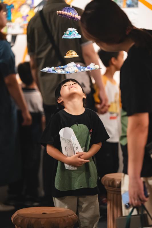 小朋友於展場中專注觀察立體創作，純真神情與藝術作品在森林飯店中交織成最動人的美學風景。
