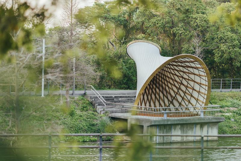 竹旋幻居。
坐落於陽明交通大學湖畔的《竹旋幻居（MemutAR）》，由香港大學建築學院副院長、高仕棠（Kristof Crolla）率領 LEAD 團隊所設計。
作品名稱「MemutAR」結合印尼語 Memutar（旋轉、循環）與 AR（擴增實境）技術，呼應其旋轉上升的竹構造型，也象徵竹構從設計、生產到組裝的跨國循環過程。整座建築先由峇里島竹工匠預製，再拆解海運至台灣，透過 AR 技術輔助定位與組裝，由台灣團隊完成重建，展現數位工具如何突破地域限制，讓高技術竹構得以跨國合作與複製。
